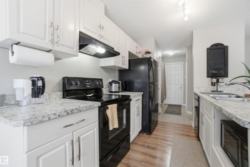 The property features a kitchen with white cabinetry, light-toned countertops, and a full suite of black appliances - 13905 138 St, Edmonton, AB - Indoor Photo Showing Kitchen With Double Sink