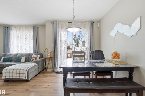 This inviting living area features warm-toned flooring, a light-colored wall, and a dining table with a dark finish - 13905 138 St, Edmonton, AB - Indoor