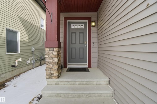 The property features a front entrance with a grey door, a stone-accented pillar, and siding in a muted tone - 13905 138 St, Edmonton, AB - Outdoor With Exterior