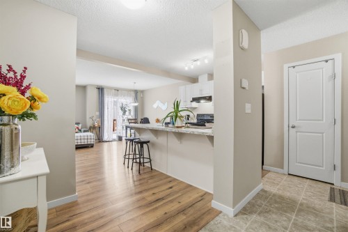 Open concept living space featuring wood-style flooring, a kitchen island with seating, and a kitchen with white cabinetry and dark appliances - 13905 138 St, Edmonton, AB - Indoor