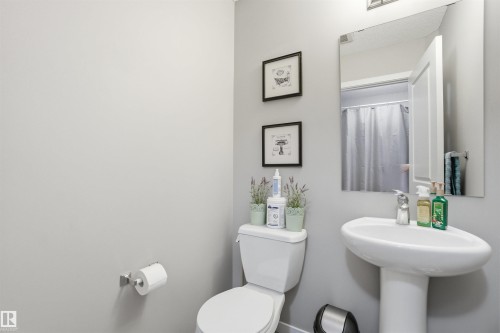 The bathroom features a pedestal sink, a toilet, and a wall-mounted mirror - 13905 138 St, Edmonton, AB - Indoor Photo Showing Bathroom