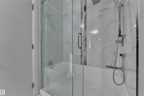 Enclosed shower and tub combination featuring clear glass doors, white tiled walls with subtle veining, a rainfall showerhead, and a handheld shower sprayer - 3702 Claxton Place, Edmonton, AB - Indoor Photo Showing Bathroom