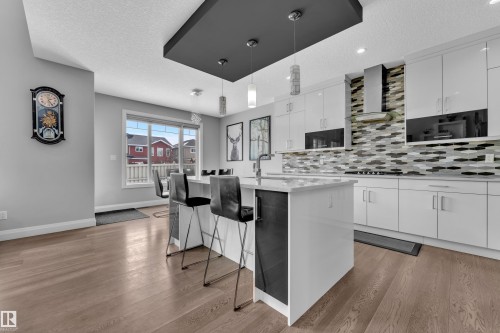 Modern kitchen featuring white cabinetry, a large center island with seating, pendant lighting, a tile backsplash, and wood-finish flooring - 3702 Claxton Place, Edmonton, AB - Indoor Photo Showing Kitchen With Upgraded Kitchen