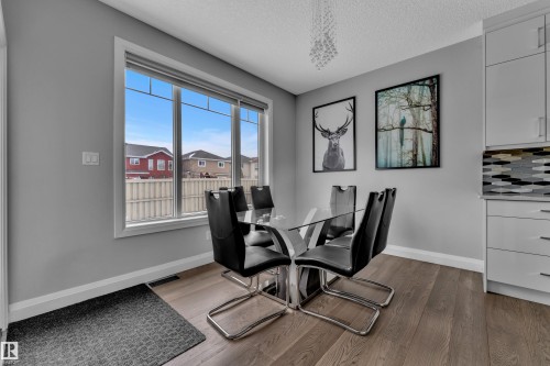Bright dining space featuring a large window with white trim, wood-finish flooring, and white wall cabinetry - 3702 Claxton Place, Edmonton, AB - Indoor