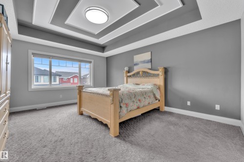 Spacious room featuring a tiered tray ceiling with a central flush-mount light fixture, large picture window, and neutral-toned carpeting - 3702 Claxton Place, Edmonton, AB - Indoor Photo Showing Bedroom