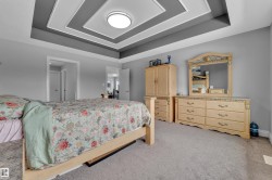 Bedroom featuring a tiered tray ceiling with recessed lighting, light gray wall paint, and gray carpeting - 