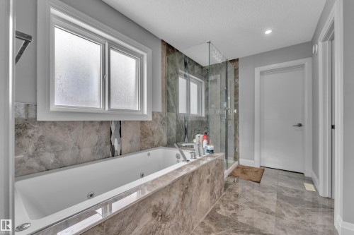 Soaking tub with integrated jets, surrounded by large format tile - 3702 Claxton Place, Edmonton, AB - Indoor Photo Showing Bathroom