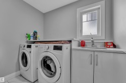 Dedicated laundry area featuring a utility sink, white cabinetry with brushed nickel pulls, and a window with frosted glass - 