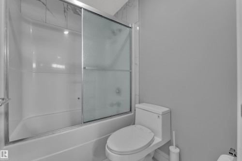 Bathtub and shower combination featuring sliding frosted glass doors - 3702 Claxton Place, Edmonton, AB - Indoor Photo Showing Bathroom