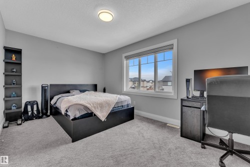 Bedroom featuring light gray walls, textured gray carpeting, a large window with white trim, and a flush-mount ceiling light - 3702 Claxton Place, Edmonton, AB - Indoor Photo Showing Bedroom