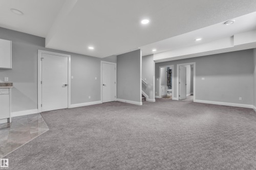 Spacious lower level featuring gray carpeting, recessed lighting, white baseboards, and a built-in cabinetry area with a stone countertop and tiled flooring - 3702 Claxton Place, Edmonton, AB - Indoor