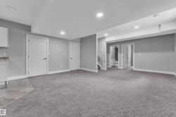 Spacious lower level featuring gray carpeting, recessed lighting, white baseboards, and a built-in cabinetry area with a stone countertop and tiled flooring - 