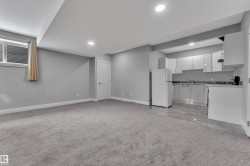 Open-concept living space featuring light gray carpet, recessed lighting, a compact kitchen with white cabinetry, a refrigerator, and a window with blinds - 