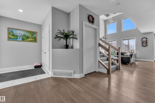 Hardwood-finish flooring extending throughout the main living areas, complemented by a carpeted staircase with light wood banisters - 3702 Claxton Place, Edmonton, AB - Indoor Photo Showing Other Room