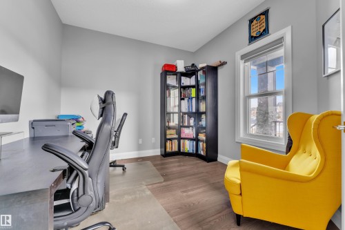 Dedicated room featuring neutral gray walls, wood-finish flooring, a double-hung window with white trim, and a built-in corner bookshelf - 3702 Claxton Place, Edmonton, AB - Indoor Photo Showing Office