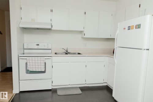 The kitchen features white cabinetry, a white electric range, a white refrigerator, a double basin sink, and a light-colored countertop - 42 11245 31 Avenue, Edmonton, AB - Indoor Photo Showing Kitchen With Double Sink