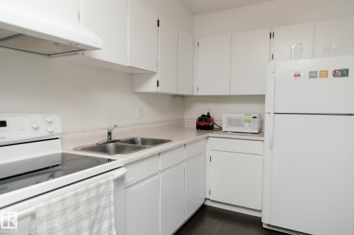 The kitchen features white cabinetry, a double basin stainless steel sink, a range with an overhead exhaust hood, and a refrigerator - 42 11245 31 Avenue, Edmonton, AB - Indoor Photo Showing Kitchen With Double Sink