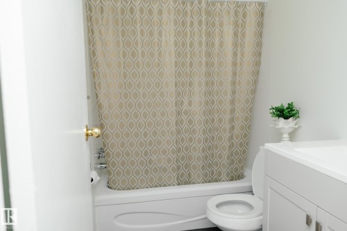 The bathroom features a bathtub with a shower, a toilet, and a vanity with a sink and storage - 42 11245 31 Avenue, Edmonton, AB - Indoor Photo Showing Bathroom