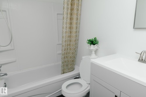 Bathroom featuring a bathtub with a shower head, a toilet, and a vanity with an integrated sink and brushed nickel faucet - 42 11245 31 Avenue, Edmonton, AB - Indoor Photo Showing Bathroom
