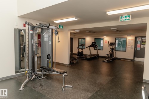Well-equipped fitness room featuring a weight machine, treadmill, elliptical, and stationary bike, all set on a dark rubberized floor - 42 11245 31 Avenue, Edmonton, AB - Indoor Photo Showing Gym Room