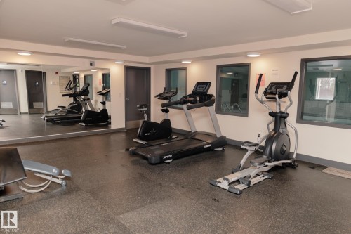Fitness room featuring a treadmill, elliptical machine, and exercise bike, complemented by a large wall mirror and windows providing natural light - 42 11245 31 Avenue, Edmonton, AB - Indoor Photo Showing Gym Room