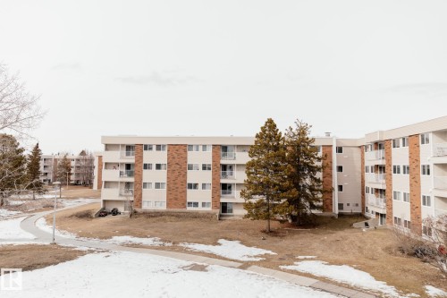 The property features exterior brick accents and balconies, set amidst an open grassy area with a paved pathway - 42 11245 31 Avenue, Edmonton, AB - Outdoor With Balcony With Facade