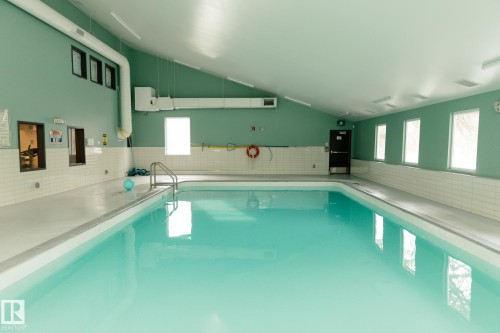 The indoor swimming pool features a light-colored tile surround, several windows providing natural light, and access to the pool via a metal ladder - 42 11245 31 Avenue, Edmonton, AB - Indoor Photo Showing Other Room With In Ground Pool