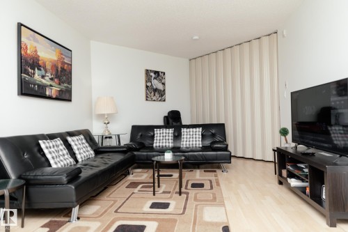 Living area featuring light-toned flooring, a patterned area rug, and a folding room divider - 42 11245 31 Avenue, Edmonton, AB - Indoor Photo Showing Living Room