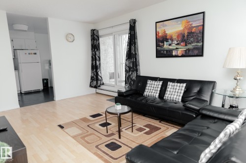 Living area featuring light wood flooring, a window with dark curtains, and a view into a kitchen with a white refrigerator and white cabinetry - 42 11245 31 Avenue, Edmonton, AB - Indoor Photo Showing Living Room