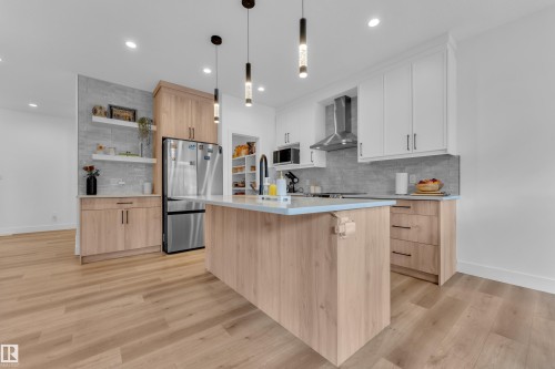 Modern kitchen featuring a light wood-finish island with pendant lighting, stainless steel appliances, white upper cabinetry, light wood-finish base cabinetry, and a tile backsplash - 9 Hunter Place, Spruce Grove, AB - Indoor Photo Showing Kitchen With Upgraded Kitchen