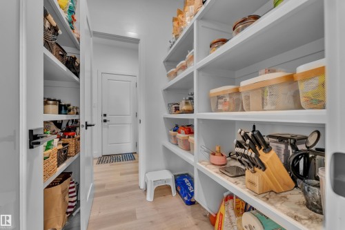 Spacious pantry featuring extensive built-in shelving, white finishes, light wood-finish flooring, and a marble-look countertop section - 9 Hunter Place, Spruce Grove, AB - Indoor