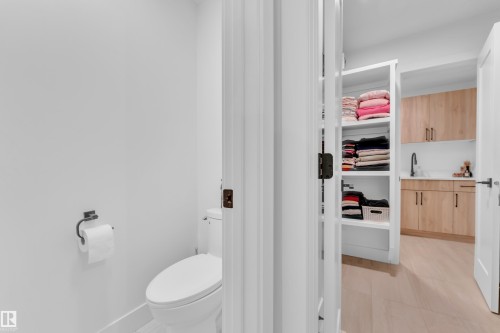 Powder room with a white toilet and matte black toilet paper holder, offering a glimpse into a utility space - 9 Hunter Place, Spruce Grove, AB - Indoor Photo Showing Bathroom