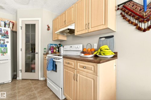 Kitchen featuring wood-finish cabinetry with silver hardware, an electric range, and a refrigerator - 8922 5Av, Edmonton, AB - Indoor Photo Showing Kitchen