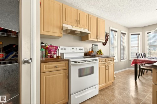 Kitchen featuring light wood-finish cabinetry, white appliances, and tiled flooring - 8922 5Av, Edmonton, AB - Indoor Photo Showing Kitchen