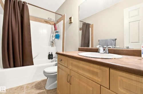 Bathroom featuring a light wood-finish vanity with an integrated sink, a large wall-mounted mirror, a tub/shower combination with tile surround, and neutral tile flooring - 8922 5Av, Edmonton, AB - Indoor Photo Showing Bathroom