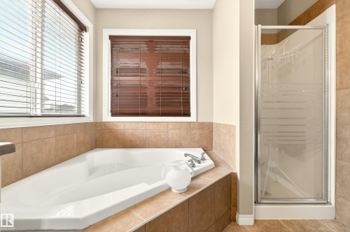 Corner soaking tub with deck-mounted chrome fixtures, surrounded by neutral-toned tile work - 8922 5Av, Edmonton, AB - Indoor Photo Showing Bathroom