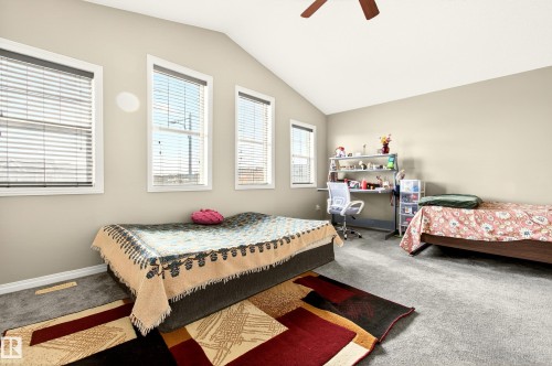 Interior room featuring vaulted ceilings, neutral wall tones, gray carpeting, multiple windows with blinds, and a ceiling fan - 8922 5Av, Edmonton, AB - Indoor Photo Showing Bedroom