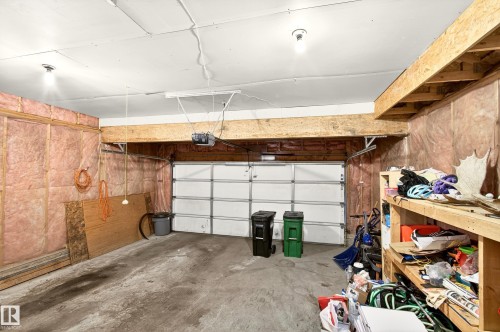 Spacious garage featuring a concrete floor, exposed insulation, a white sectional garage door with opener, and overhead lighting - 8922 5Av, Edmonton, AB - Indoor Photo Showing Garage