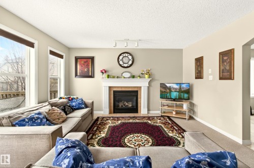 Living area featuring a white mantel fireplace with a dark tile surround, track lighting, and beige carpeting - 8922 5Av, Edmonton, AB - Indoor Photo Showing Living Room With Fireplace