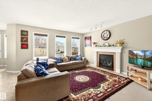 Living area featuring a white mantel fireplace with tile surround, multiple windows, track lighting, and light-toned wall paint - 8922 5Av, Edmonton, AB - Indoor Photo Showing Living Room With Fireplace
