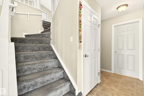 Carpeted staircase with white railings, complemented by ceramic tile flooring in the entry area - 8922 5Av, Edmonton, AB - Indoor Photo Showing Other Room