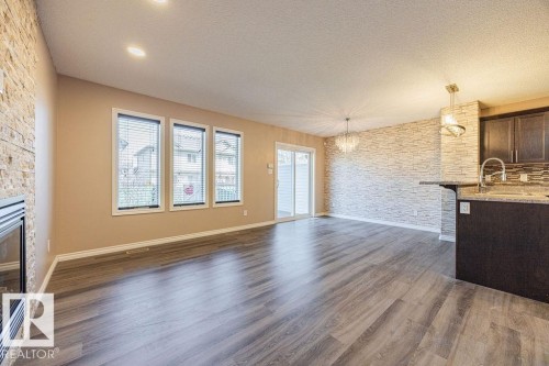 Open-concept living space featuring wood-finish flooring, a stacked stone accent wall, and a built-in fireplace - 14 9350 211 Street, Edmonton, AB - Indoor Photo Showing Kitchen