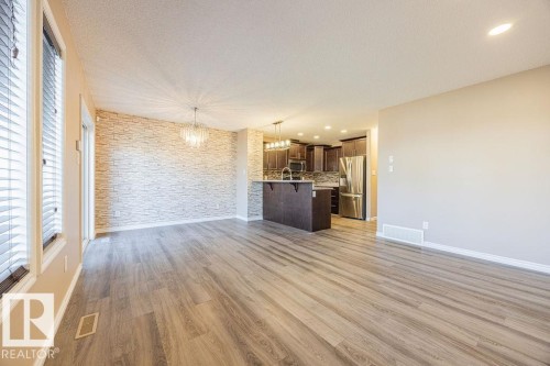 Open-concept living space featuring wood-finish flooring, a decorative stone accent wall, and a crystal chandelier - 14 9350 211 Street, Edmonton, AB - Indoor