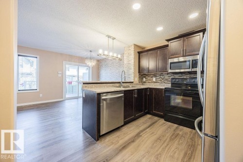 Kitchen featuring dark wood cabinetry, stainless steel appliances, and a stone-look countertop - 14 9350 211 Street, Edmonton, AB - Indoor Photo Showing Kitchen With Upgraded Kitchen