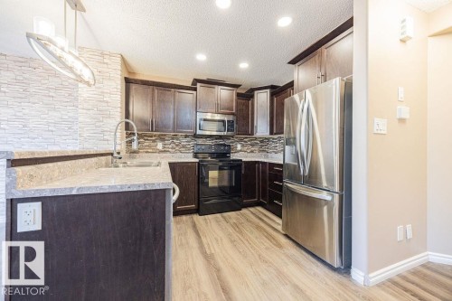 Kitchen featuring wood-finish flooring, dark wood cabinetry, stainless steel appliances, and light-colored countertops - 14 9350 211 Street, Edmonton, AB - Indoor Photo Showing Kitchen With Upgraded Kitchen