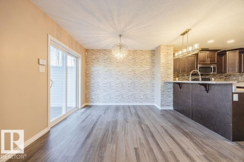 Open-concept living area featuring wood-finish flooring, a textured accent wall, and a crystal chandelier - 14 9350 211 Street, Edmonton, AB - Indoor Photo Showing Kitchen
