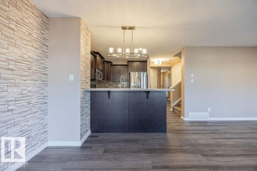 Open-concept living space featuring wood-finish flooring, a contemporary chandelier, and a breakfast bar with a stone-look countertop - 14 9350 211 Street, Edmonton, AB - Indoor Photo Showing Kitchen
