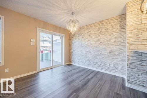 Spacious room featuring wood-finish flooring, a full wall with stacked stone veneer, and a sliding glass patio door - 14 9350 211 Street, Edmonton, AB - Indoor Photo Showing Other Room