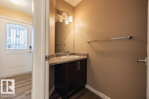 Powder room featuring a dark wood vanity with a light-colored countertop, an oval undermount sink, and a contemporary three-bulb vanity light - 14 9350 211 Street, Edmonton, AB - Indoor Photo Showing Bathroom