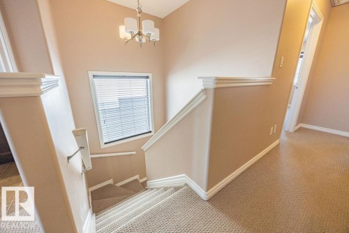 Carpeted staircase with white trim, a landing window featuring blinds, and a brass-tone chandelier - 14 9350 211 Street, Edmonton, AB - Indoor Photo Showing Other Room